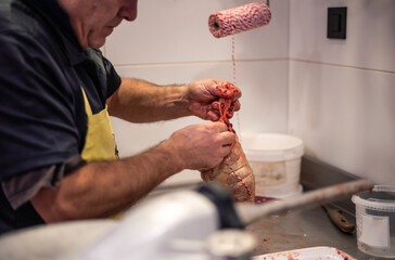 Closeup of Butcher's Blood-Stained Hands Tying Stuffed Chicken with Rope