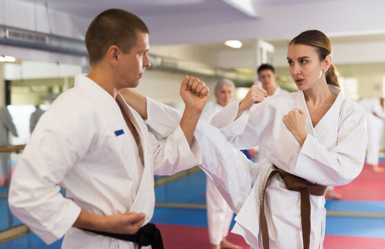 Man and woman in kimono and belt fighting with opponent during group karate training.