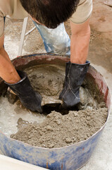 Man bricklayer stirring cement and sand mixture with water to make concrete in container. Close up. Latam