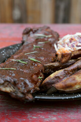 Overhead view of pork ribs marinated with barbecue sauce and herbs, sweet potato fries and coleslaw salad, in a black dish on the table.	