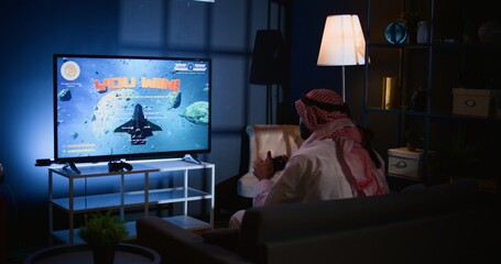 Middle Eastern gamer plays intense classic arcade space shooter videogame. Man relaxing at home...