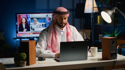 Arab businessman starting his day working from home, opening laptop, surfing the net. Middle...