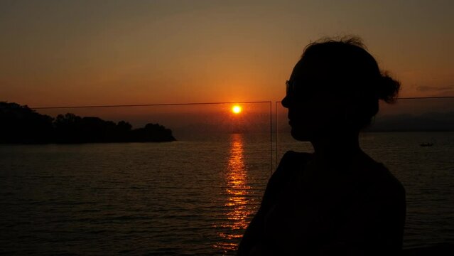 Lady silhouette admire sunset bright sun. A view of female silhouette against sea landscape during nightfall time.