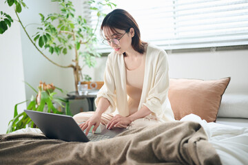 ベッドでノートパソコンを使う20代女性
