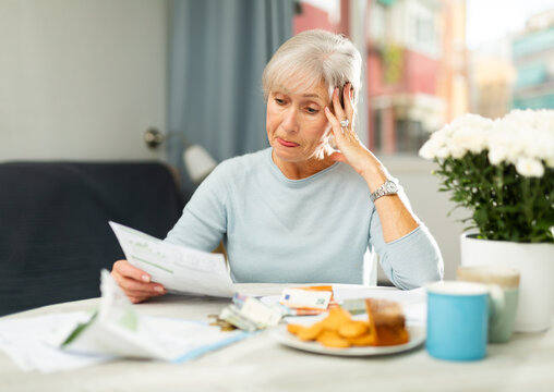 Grey haired thoughtful woman sitting at table and analysing financial documents. High quality photo