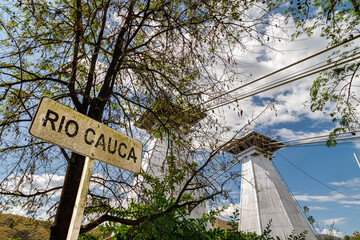 Cauca River sign with Western Suspension Bridge in the background in Santa Fe de Antioquia, Colombia