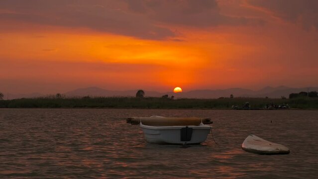 Surfing boat on evening waves at nightfall. A view of alone silhouette of surfing boat against orange and red sky during nightfall time.