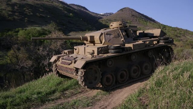 Old panzer 3 tank moving over dirt hill in canyon - wide, panning shot