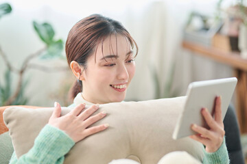 ソファでくつろぎながらタブレット端末を見る女性