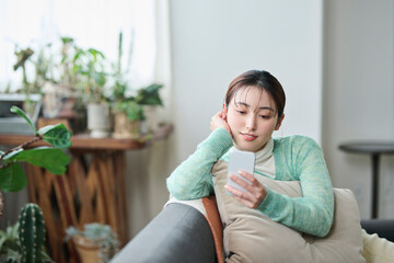 ソファでくつろぎながらスマートフォンを見る女性
