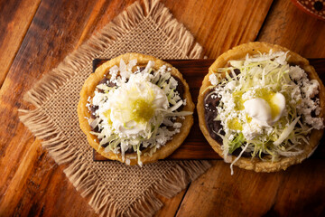 Sope. Traditional homemade Mexican food prepared with flattened and pinched on the border fried corn dough covered with refried beans, green or red sauce, lettuce, cheese, onion and sour cream. - 763626981