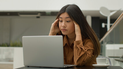 Exhausted overworked Asian chinese japanese woman student girl studying online with laptop in cafe...