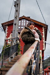 Brunette woman in green coat, scarf, gloves, gazes at vibrant red rural house.