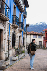Fototapeta na wymiar Young Peruvian man in camo coat, brown sling bag, strolls amidst vibrant, stone rural houses.