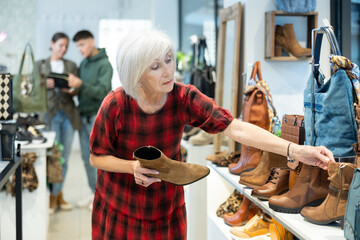 Elderly woman in casual clothes chooses ankle boots in store..