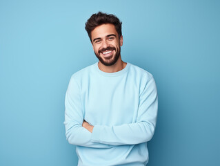 Hombre latino, joven, atractivo y con barba corta, feliz, usando ropa casual de color azul posando sobre un fondo del mismo color