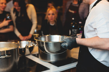 Group of guests in a cooking class studio, adults preparing different dishes in the kitchen together, people in aprons learn on culinary master class, chef uniform, hands in gloves, italian cuisine - obrazy, fototapety, plakaty