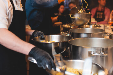 Group of guests in a cooking class studio, adults preparing different dishes in the kitchen together, people in aprons learn on culinary master class, chef uniform, hands in gloves, italian cuisine