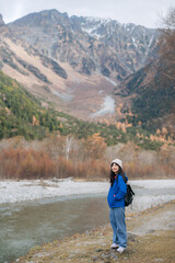 Success on the horizon, Asian woman in a blue jacket stands by a cliff, enjoying nature's beauty. A portrait of a traveler's happiness and achievement.