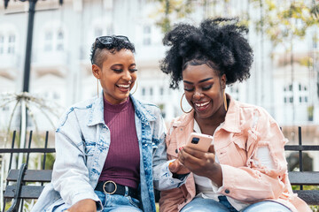 black women friends using smartphone having fun in the city - obrazy, fototapety, plakaty