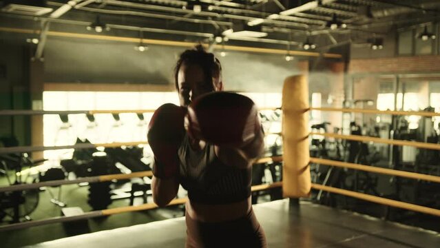 A female boxer channels intensity and precision as she throws direct punches towards the camera, training in the gym with a spirit that showcases her powerful fighting technique