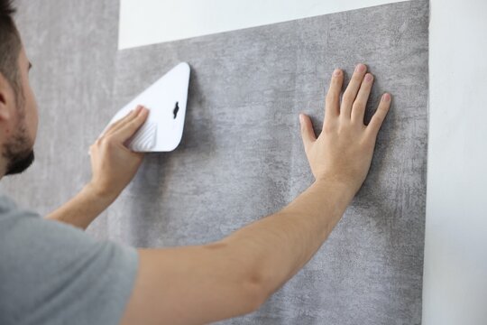 Man smoothing stylish gray wallpaper in room