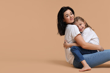 Beautiful mother with little daughter sitting on beige background. Space for text