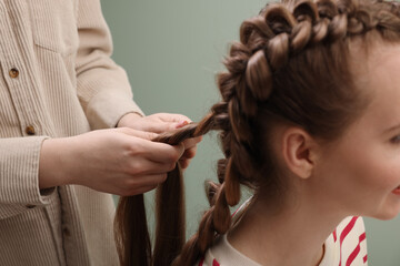 Professional stylist braiding woman's hair on olive background, closeup