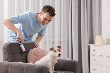 Smiling man removing pet's hair from armchair at home. Space for text