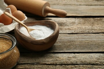 Baking powder, eggs, brown sugar and rolling pin on wooden table, closeup. Space for text