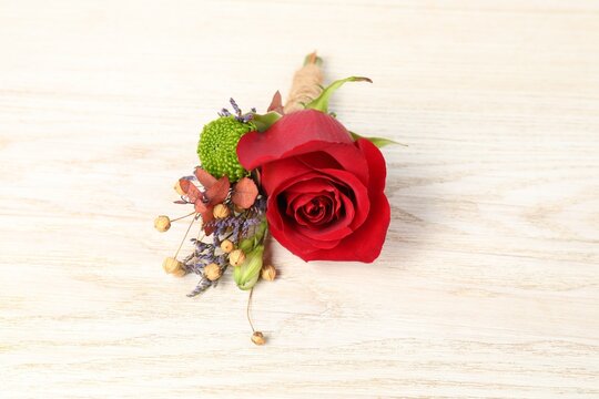 Stylish boutonniere with red rose on light wooden table, closeup