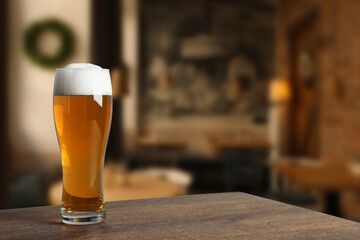 Glass with fresh beer on wooden table in pub, space for text