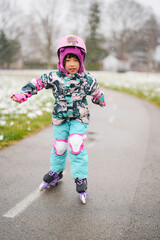 Happy Asian girl kid wearing snow suit and safety guard helmet having fun while playing rollerblade in the park in snowing winter season. 
