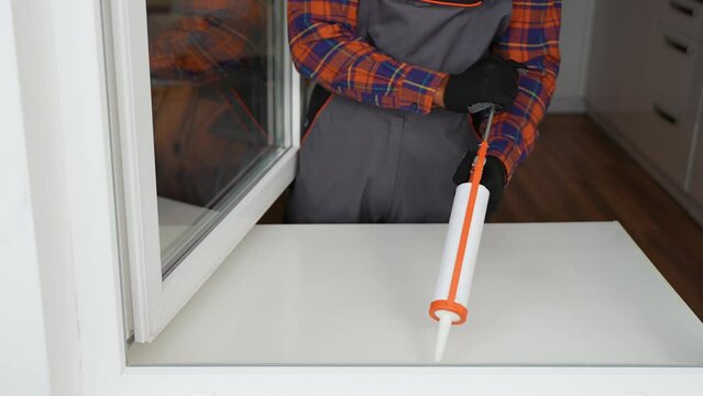 A worker is applying polyurethane foam to fill gap between sash and window frame
