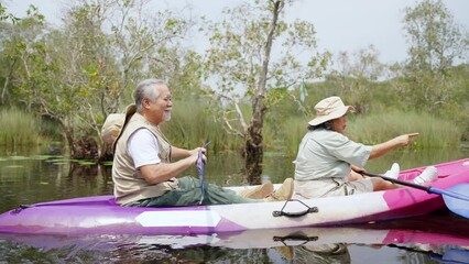 Happy Asian family senior couple enjoy and fun outdoor lifestyle travel nature kayaking in the river at mangrove forest on summer holiday vacation. Elderly people mental health and ecotourism concept.