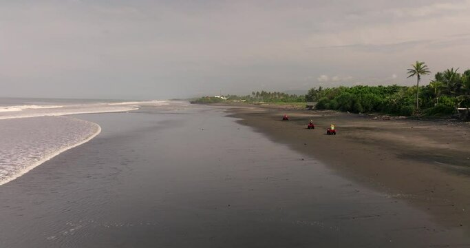 Tourist activity as red ATVs ride on black sand beach of Bali, Indonesia. Aerial