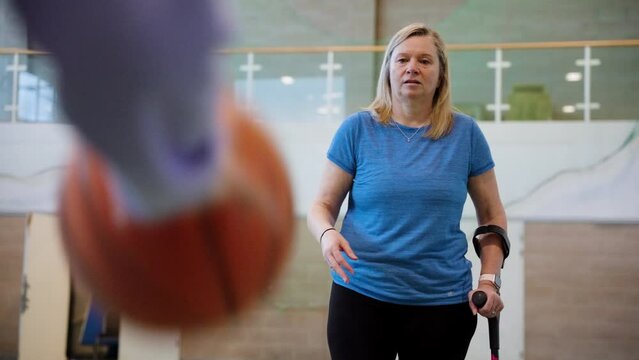 Woman using crutches while dribbling a basketball around opponent
