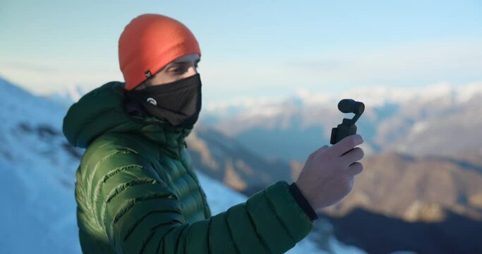 videographer with orange colored hat and green jacket on holiday in high mountains does selfie with DJI Osmo Pocket
