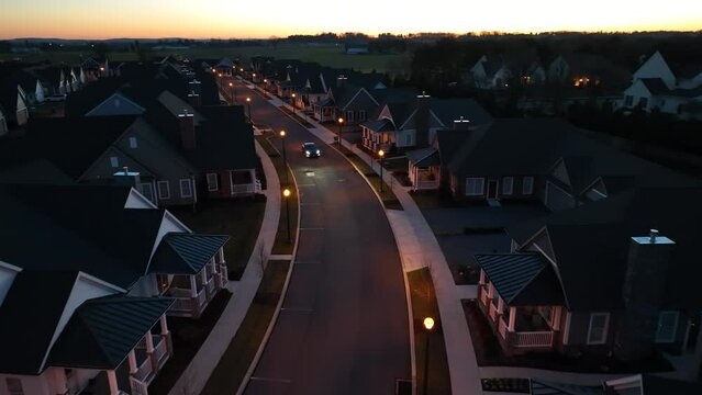 Car driving through modern 55+ retirement neighborhood during sunset. Electric Tesla Model Y passing drone at night.