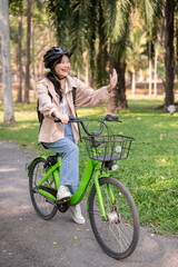A happy young Asian female college student is enjoying riding her bike in a green park.