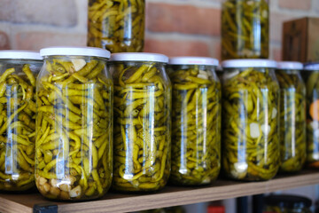 Pickled green beans in glass jars. Glass jars filled with pickled green beans are lined up on a wooden shelf.