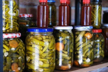 Assorted Pickled Vegetables and Sauces in Jars. A variety of pickled vegetables and red sauces in jars on a wooden shelf against a brick wall.
