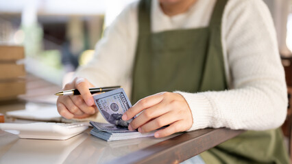 A cropped shot of a female small business owner managing her shop budget, calculating, counting cash