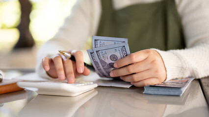 A cropped shot of a female small business owner managing her shop budget, calculating, counting cash
