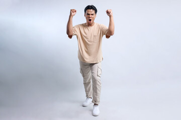 Excited young man wearing casual clothes raise fist celebrating victory and show winning gesture....