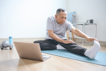 Senior man in sportswear doing stretching workout while watching online tutorial sport video via laptop at home - obrazy, fototapety, plakaty