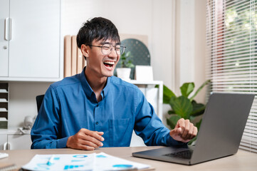 Fototapeta premium job, manager, occupation, freelance, student, corporate, smile, businessman, employee, office. A man is sitting at desk with laptop, stack papers and smiling. He is wearing a blue shirt and glasses.