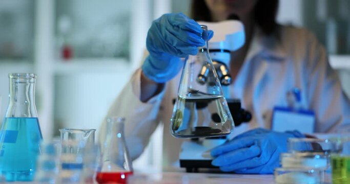 Lab technician stirs liquid in beaker with circular motions