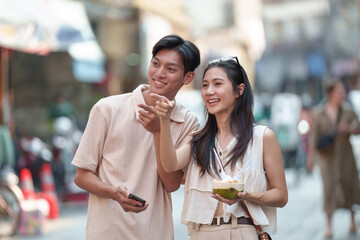 A cute and happy Asian tourist couple tours the old town market using their phone to find directions. Tourist attractions, shops, street food, traveling together. backpacker Holiday travel concept.