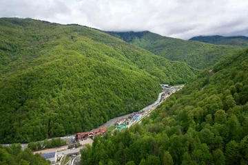 Fotobehang View of the Rosa Khutor ski resort and the Mzymta River from a gondola lift to the top of the Rosa Peak of the Caucasus Mountains on a spring day, Krasnaya Polyana, Sochi, Krasnodar Territory, Russia © Ula Ulachka